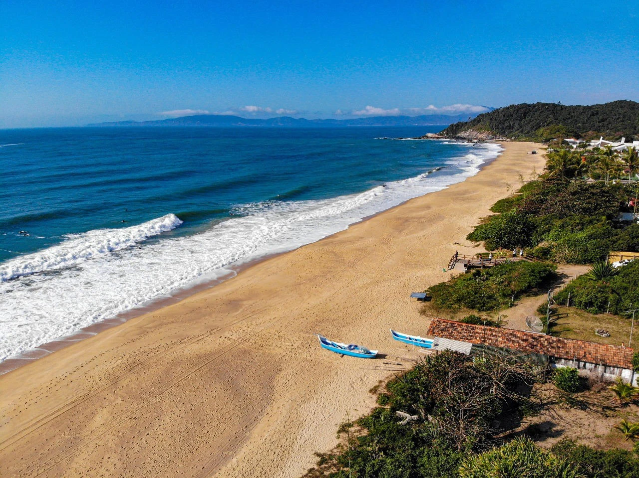 Praia do Estaleirinho, com um céu sem nuvens e um mar azul escuro.